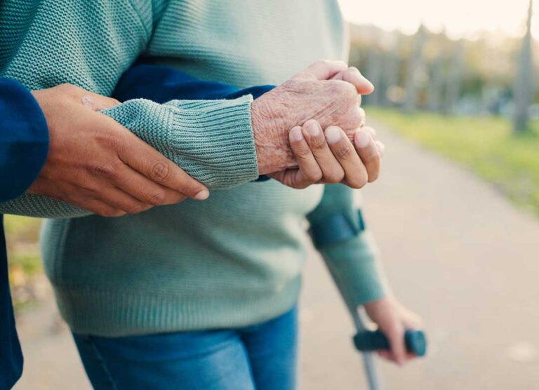 Older adult speaking with a caregiver in a bright assisted living room with luggage and personal items nearby.
